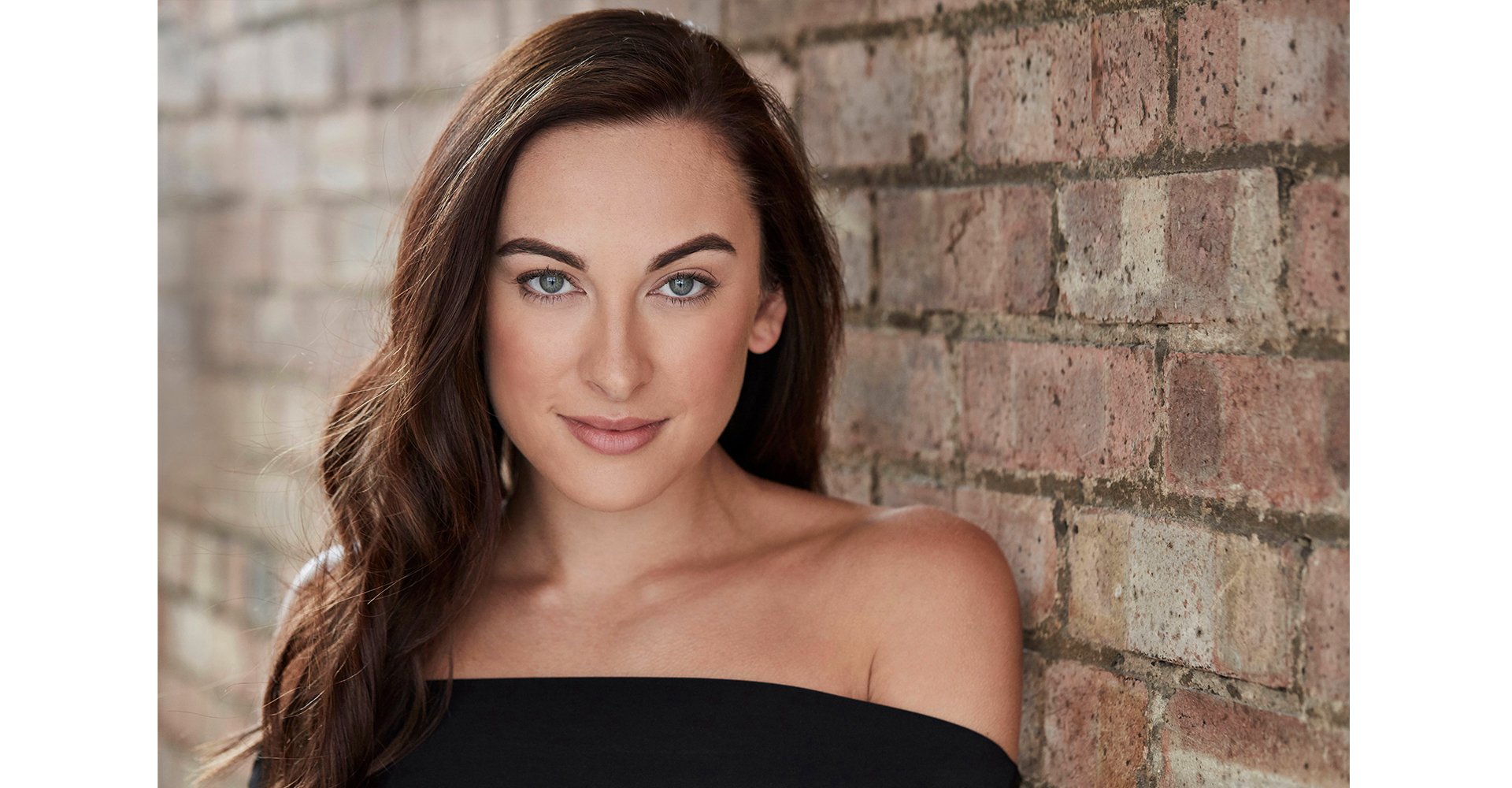 Actress dancer with brown hair headshot portrait standing front brick wall in natural light